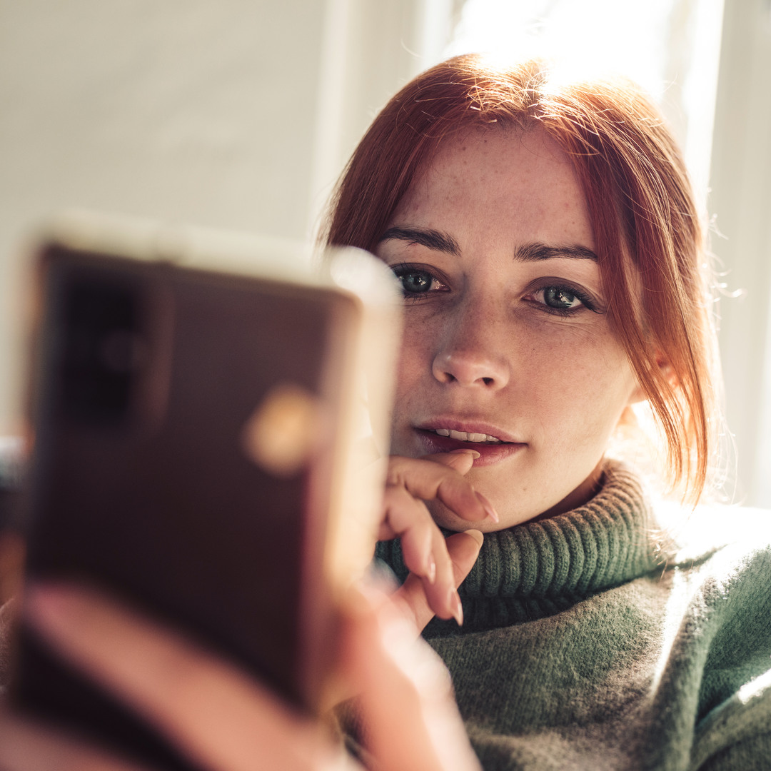 Rödhårig tjej som sitter med sin telefon i handen